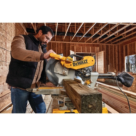 12 inch double bevel sliding compound miter saw being used to cut a thick piece of wood by a worker.